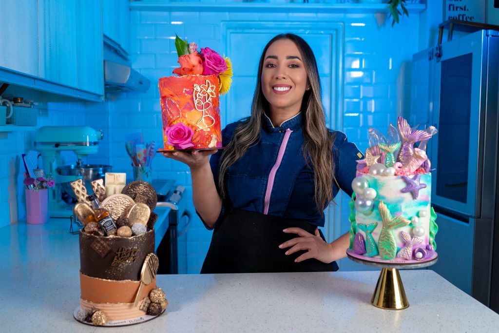 Bel García en su cocina sosteniendo el pastel Floral Chic, junto al Chocolate Lover Cake y el Mermaid Fantasy Cake